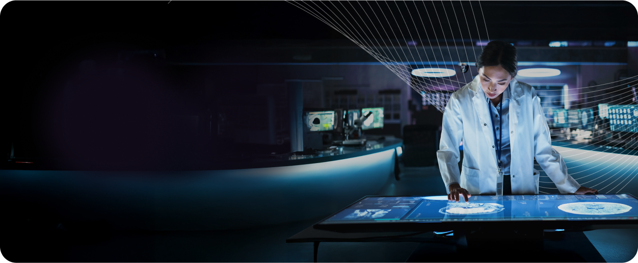 A scientist in a lab coat interacts with a touchscreen table displaying data and images, surrounded by high-tech equipment in a dimly lit lab.
