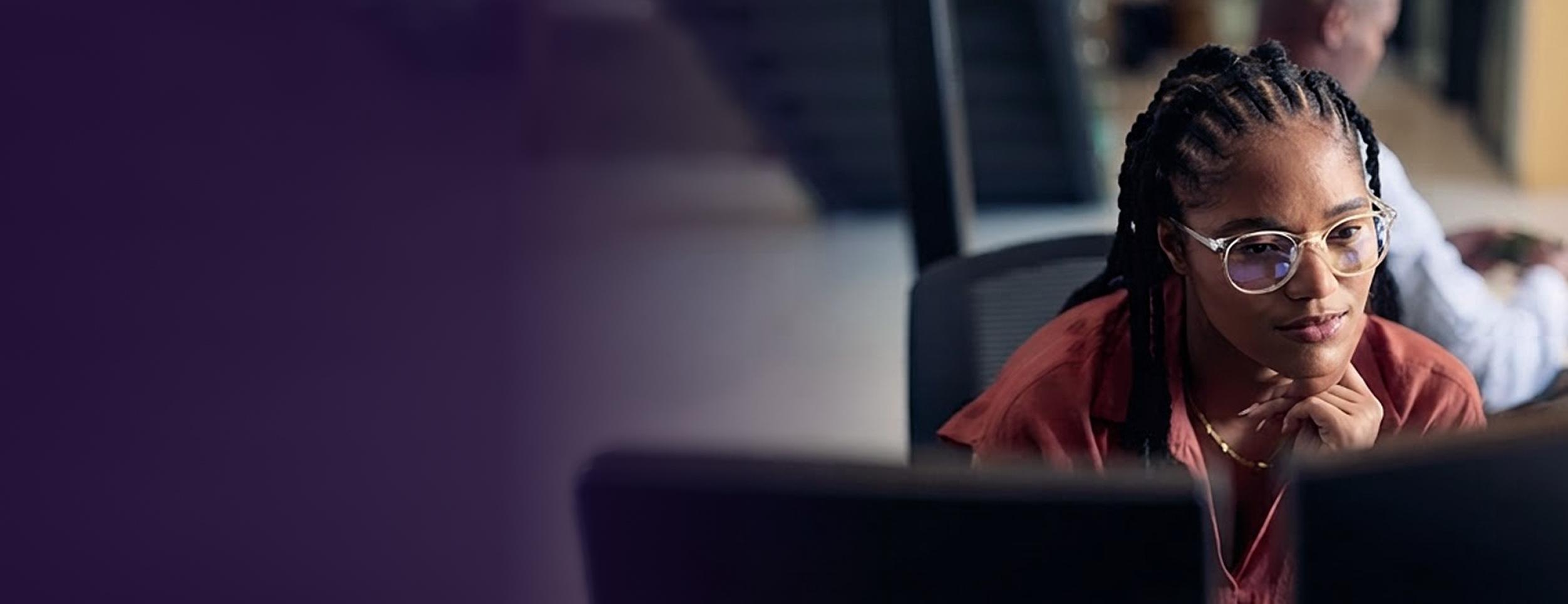 A person wearing glasses and a red shirt is focused on a computer screen in an office setting.