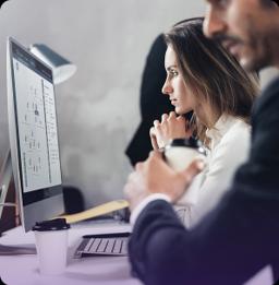 Two people working at computers in a modern office, one focusing on a screen displaying diagrams, the other holding a coffee cup.