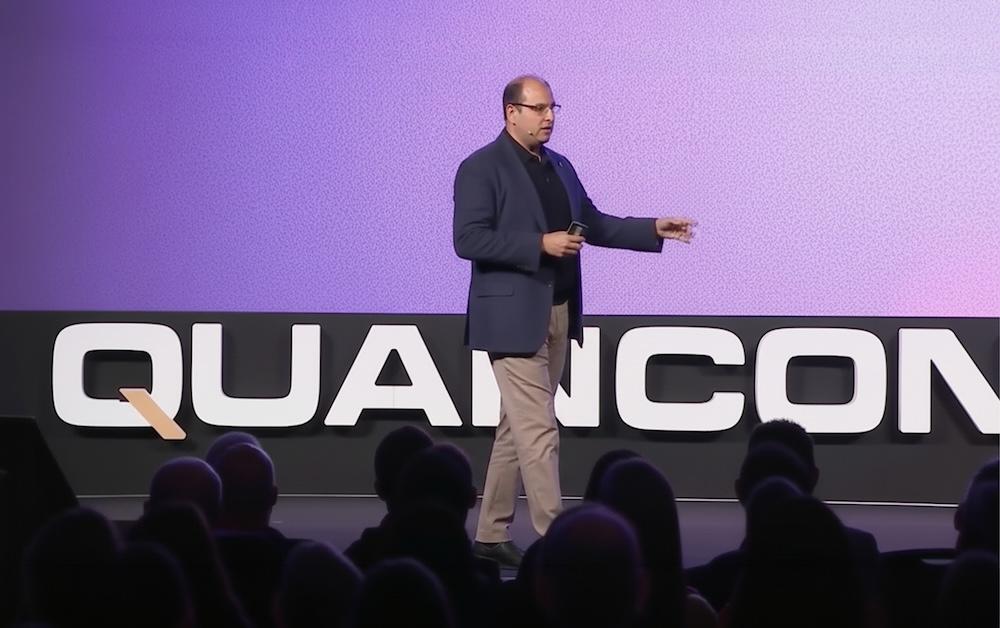 Vishal Marria in a suit gestures during a presentation on stage, with a purple-lit background and "QUANCON" partially visible.
